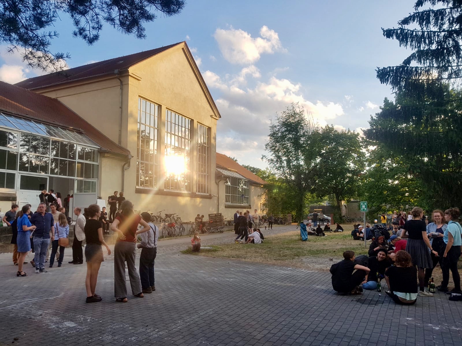 Innenhof der Hochschule an der Pfotenhauerstraße während der Jahresausstelung. Menschen sitzen im Gras, trinken und unterhalten sich.